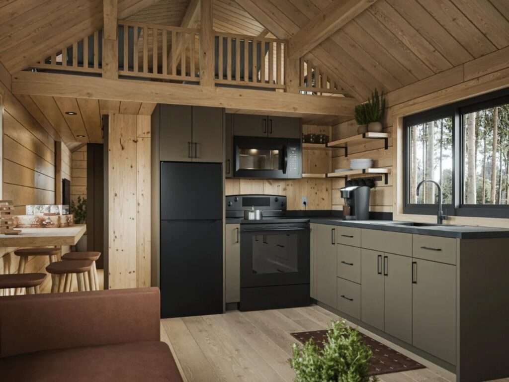 Modern cabin kitchen with olive-green lower cabinets, black appliances, solid wood walls, and a view of the open upper loft floor above.