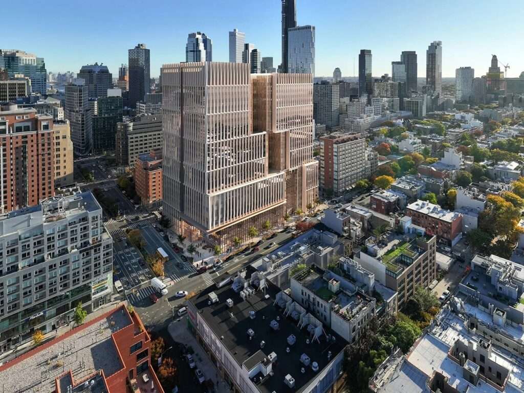 Aerial view showing the Manhattan Detention Center high-rise tower set within the dense neighborhood fabric.