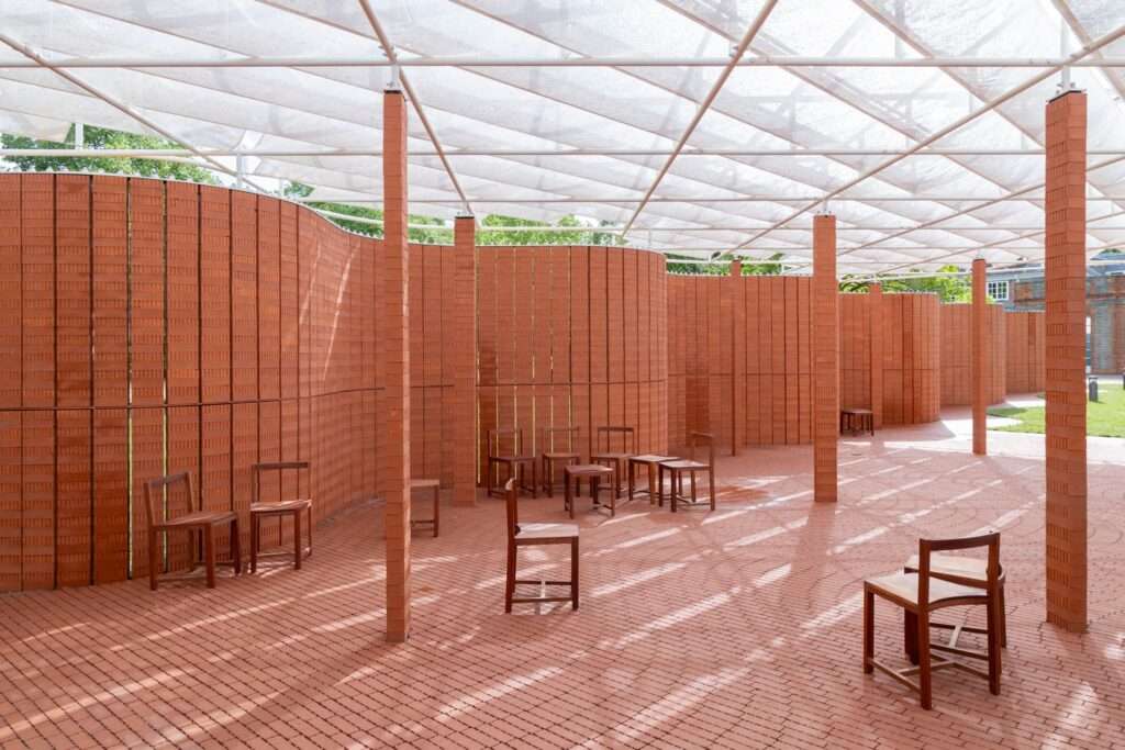 Interior of Serpentine Pavilion showing curved brick walls wooden chairs and dappled light