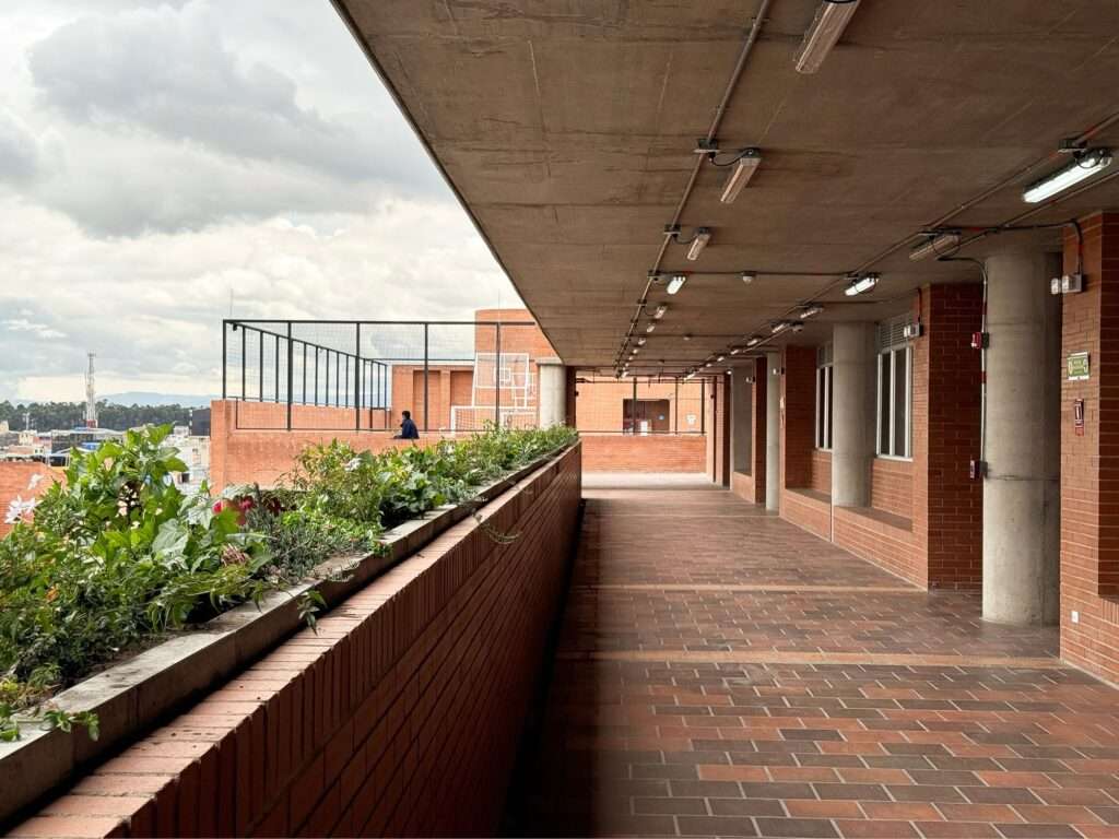 Semi-open outdoor hallway with brick planters and concrete ceiling at Feliza Bursztyn School.