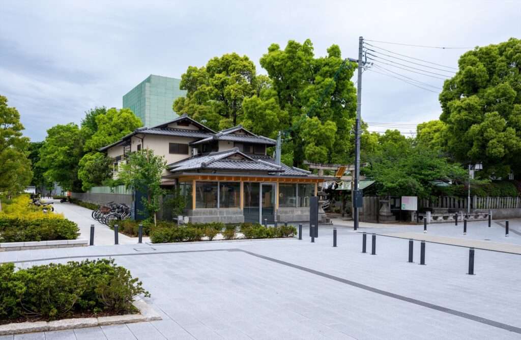 Wide shot of Cafe N+ integrated into a large paved public plaza with greenery, bicycles, and historical buildings in the background.