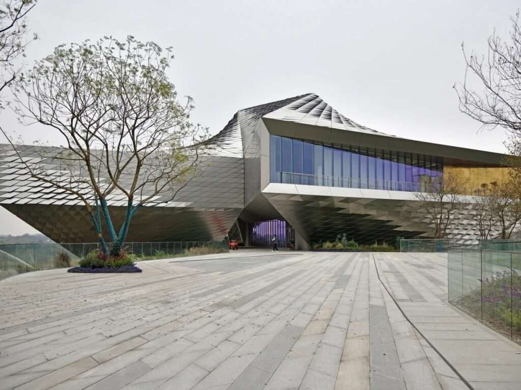 Frontal perspective of Chengdu Pavilion showing its metallic skin, cantilevered second floor, and open ground-level walkway.