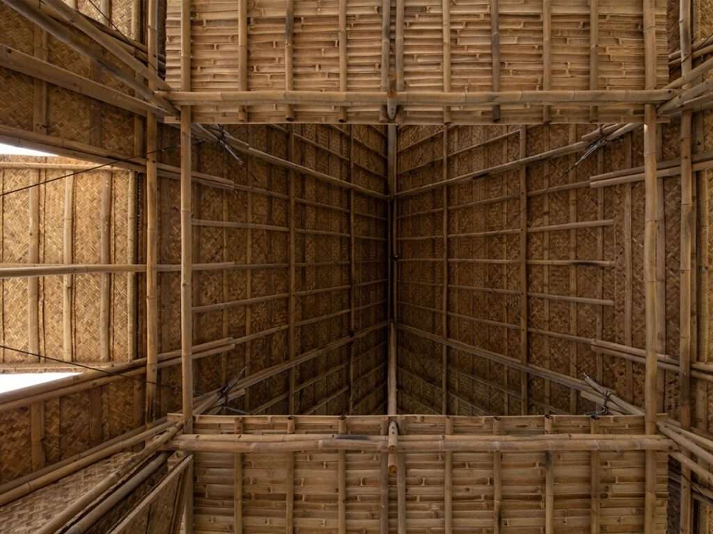 Overhead view of the entire interior of the Floating Bamboo House, taken from a high corner, looking across the main floor and up into the complex bamboo framework of the roof structure.