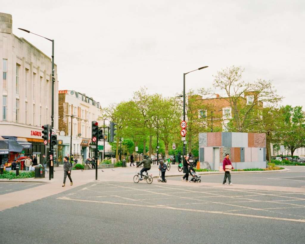 Pedestrians and cyclists crossing the road junction near the Maida Hill stone pavilion in London.