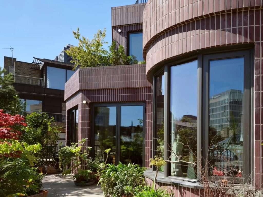 Landscaped outdoor rooftop terrace with potted plants and large glass bay windows set into dark brick walls.