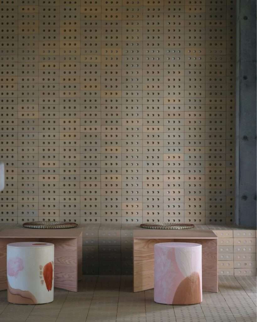 Seating area with perforated block wall, wooden low tables, and handcrafted pastel ceramic stools.