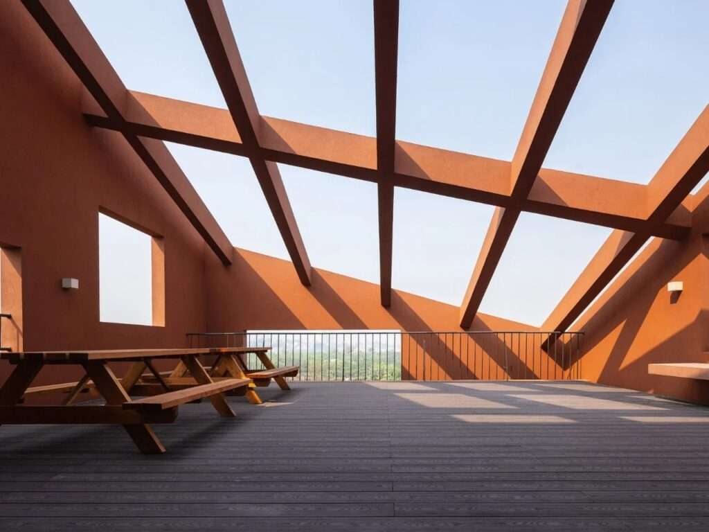 Rooftop terrace with wooden picnic tables under an open terracotta pergola structure casting angular shadows on deck flooring.