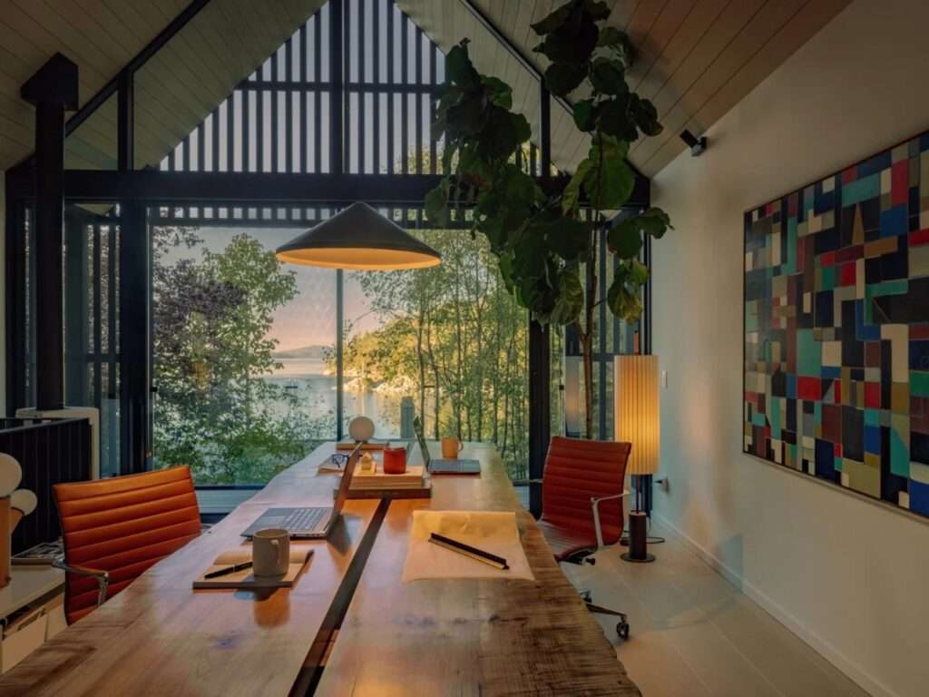 Interior of Forest Studio looking out large floor-to-ceiling glass doors toward the surrounding trees and distant body of water.