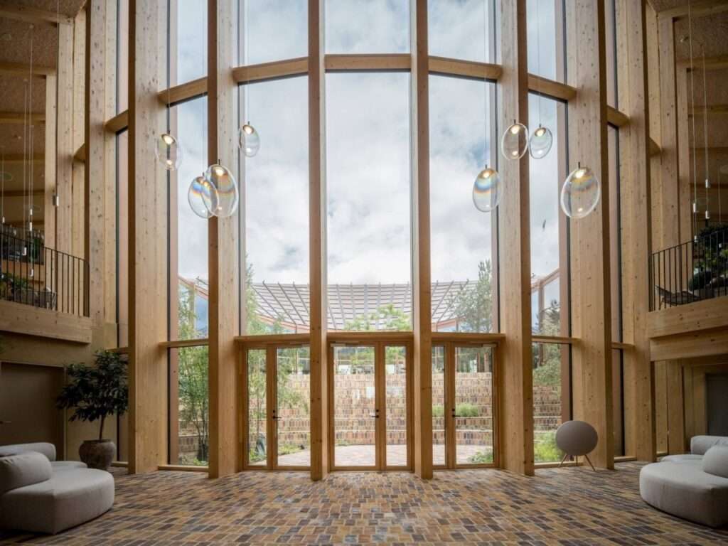 Bright double-height lobby with mass timber columns, decorative hanging glass orb light fixtures, and large glass doors leading to the courtyard.