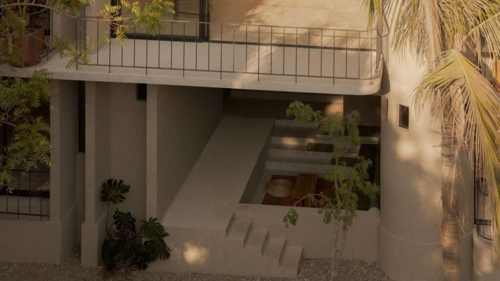 Sunlit outdoor lounge pit with concrete steps, wooden table, and tropical plants underneath an overhanging balcony terrace.