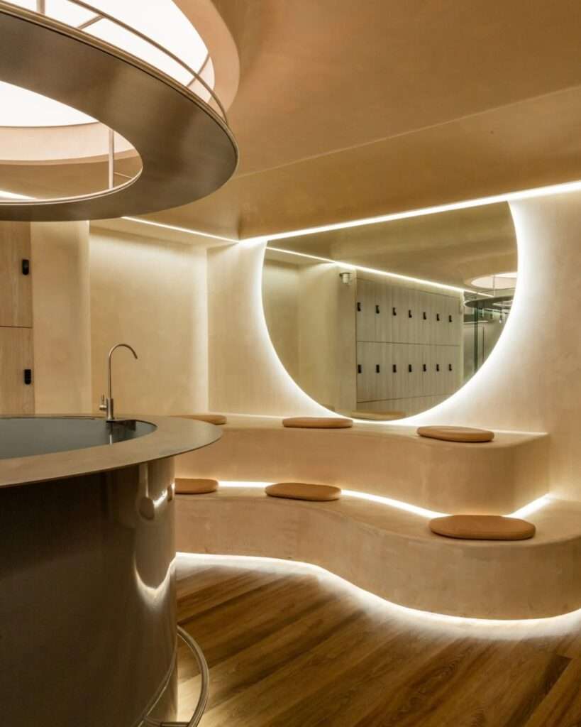 Curved plaster bench seating with warm concealed lighting below a large backlit semi-circular mirror in the reception lounge.