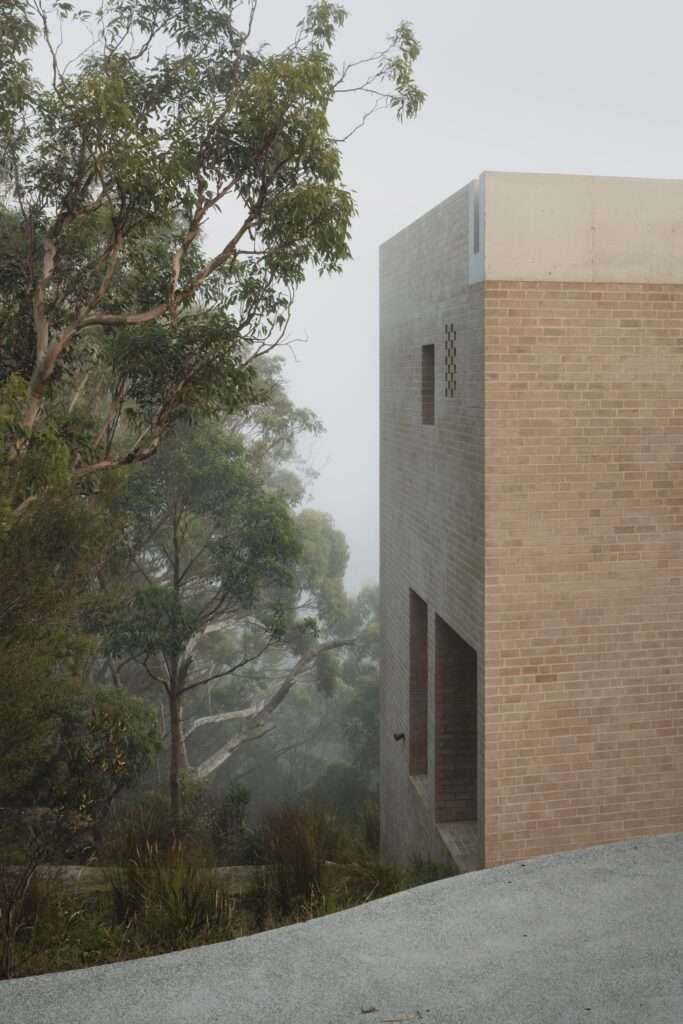 A close-up of the clean-lined brick facade and concrete roof element of EA House against a backdrop of eucalyptus trees and heavy mist.