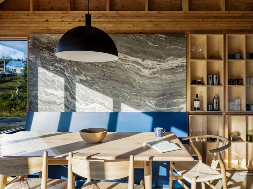 Dining area in Skybox residence featuring a wooden dining table, blue built-in bench, marble accent wall, and custom open shelving.
