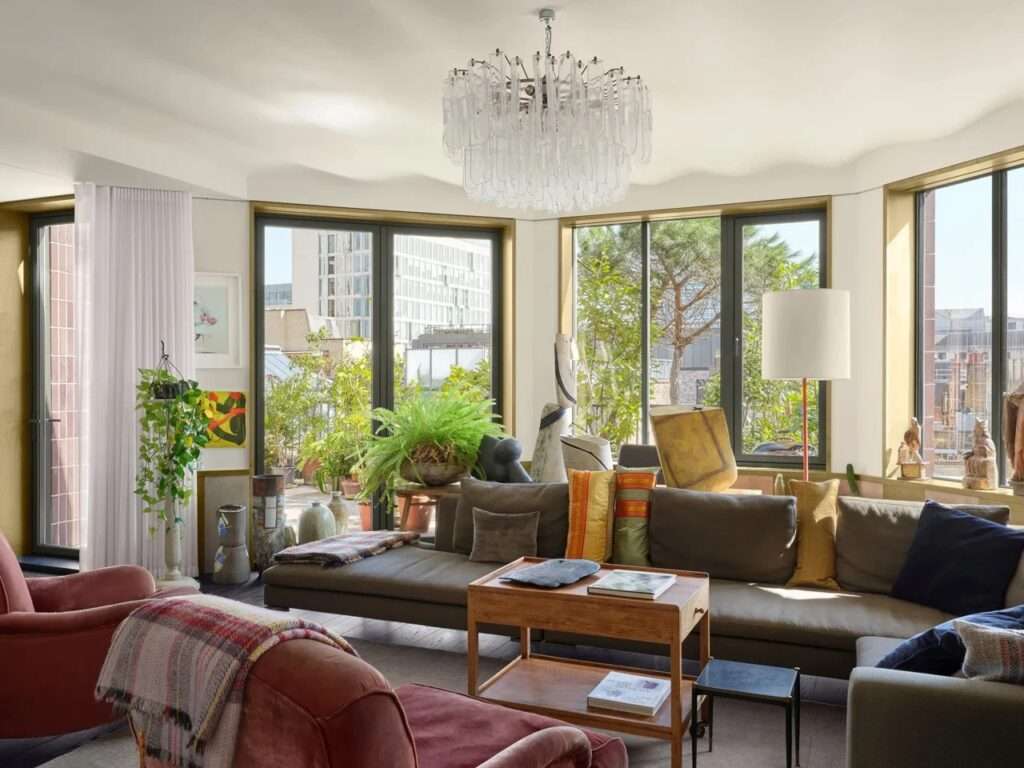 Open-plan interior living room with comfortable seating, modern chandelier, and large windows opening onto a garden terrace.