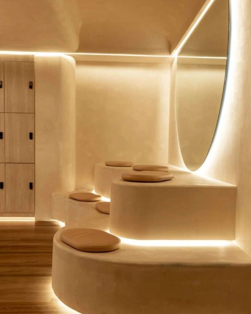 Tiered plaster bench seating with warm LED perimeter illumination alongside natural wood lockers.