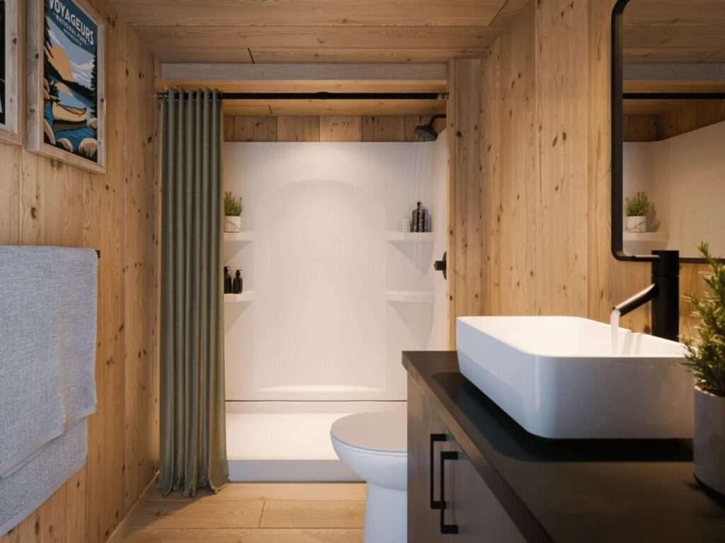 Compact wooden bathroom featuring a white vessel sink on a dark vanity, modern black faucet, white toilet, and walk-in shower enclosure.