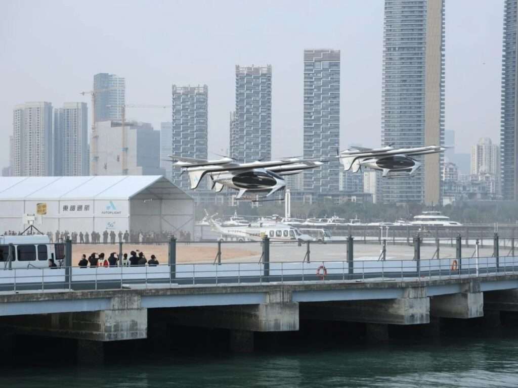 Two AutoFlight eVTOL aircraft taking off from a vertiport near a body of water, with city skyscrapers in the background.