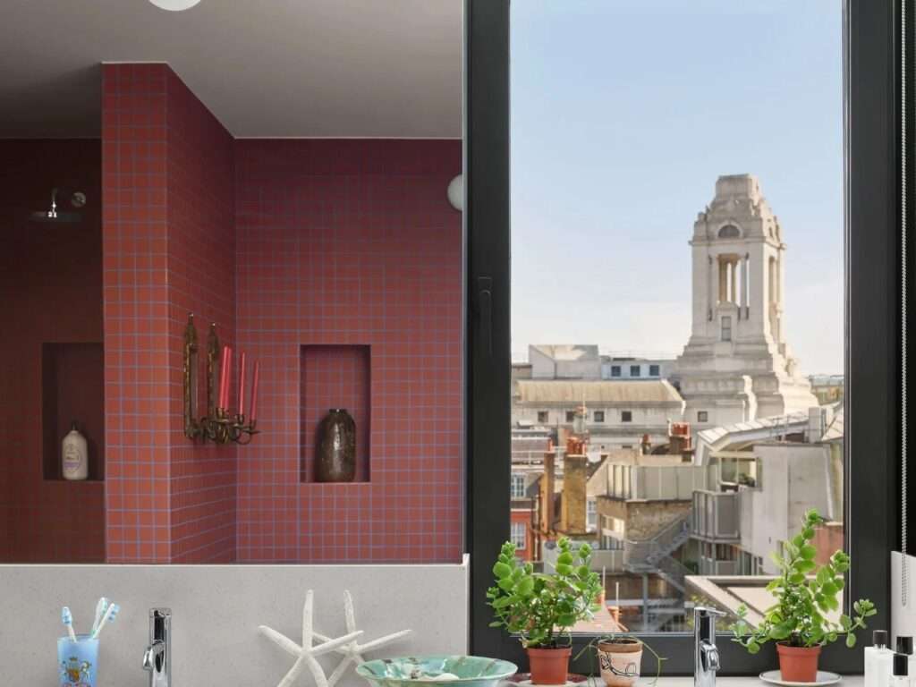 Bathroom interior with red square ceramic tiles and a large window framing historic London landmarks.