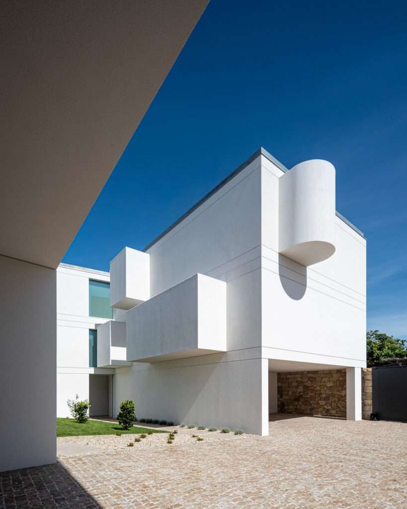Courtyard view of a modern white building featuring cantilevered box-like balcony projections and a curved wall detail.