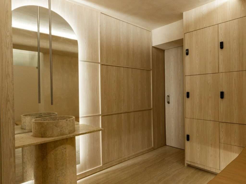 Travertine stone sink vanity and tall light oak locker cabinets in a well-lit studio changing room.