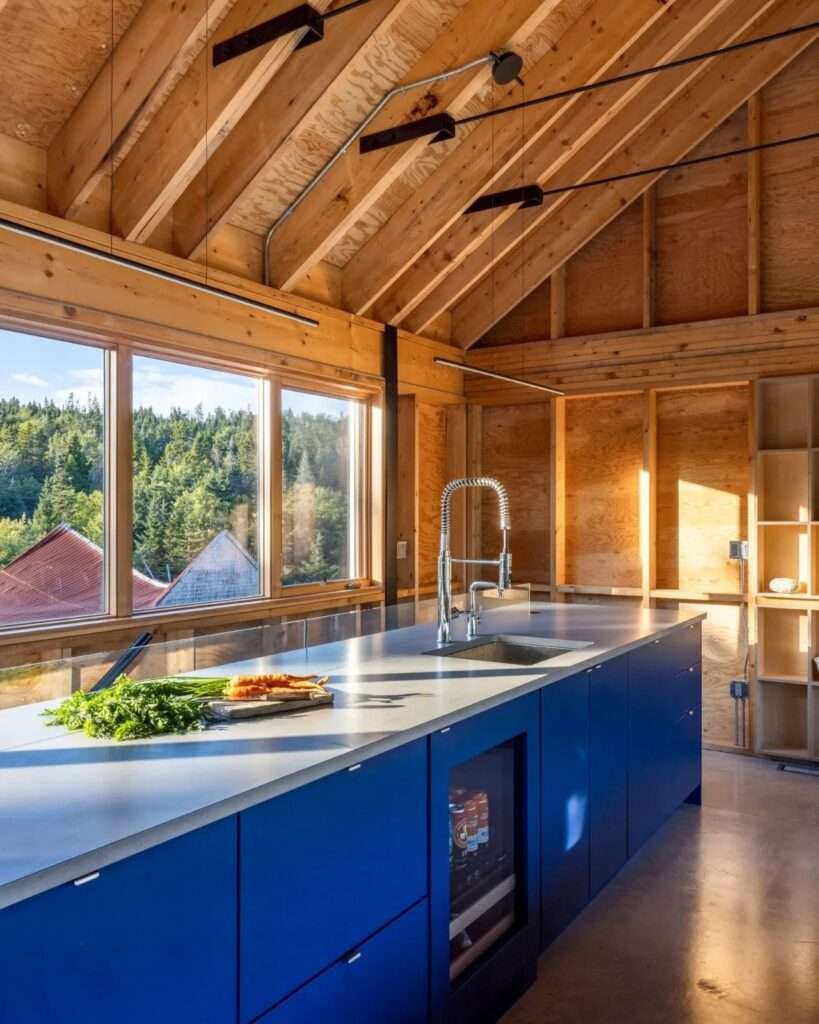 Kitchen island with deep blue cabinetry, stainless steel faucet, and large window overlooking the surrounding forest canopy.