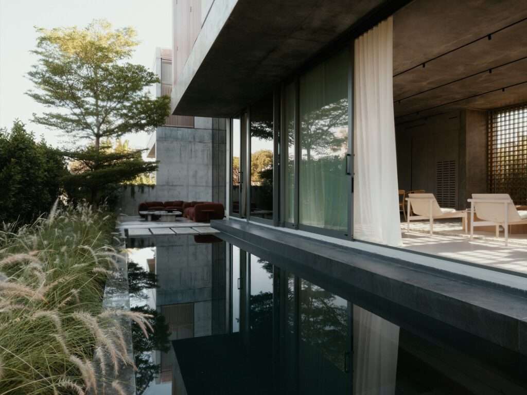 Outdoor reflection pool reflecting the concrete structure and lush greenery next to a covered lounge patio.