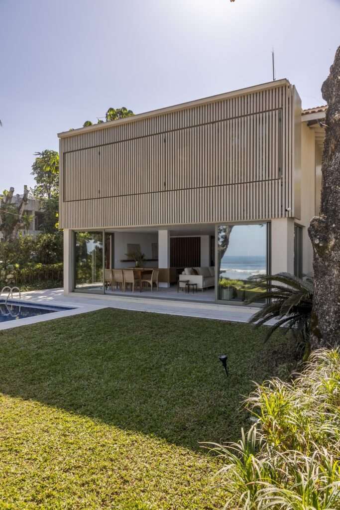 Perspective view of Casa ADS showing the fully closed slatted timber upper facade and open ground level living room adjacent to the lawn.
