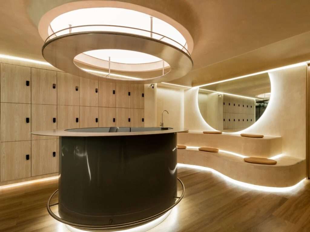 Cylindrical olive green reception desk under a circular skylight fixture in a modern minimalist lobby.