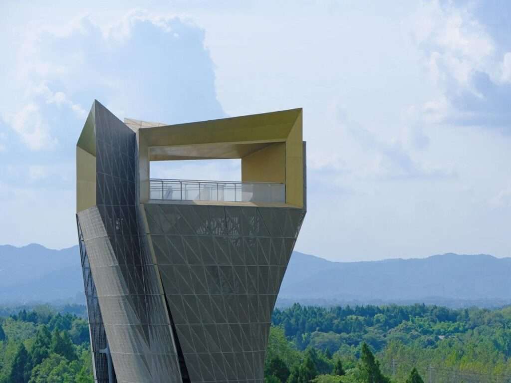 Vertical metallic observation tower with a golden open-air viewing deck against a blue sky.