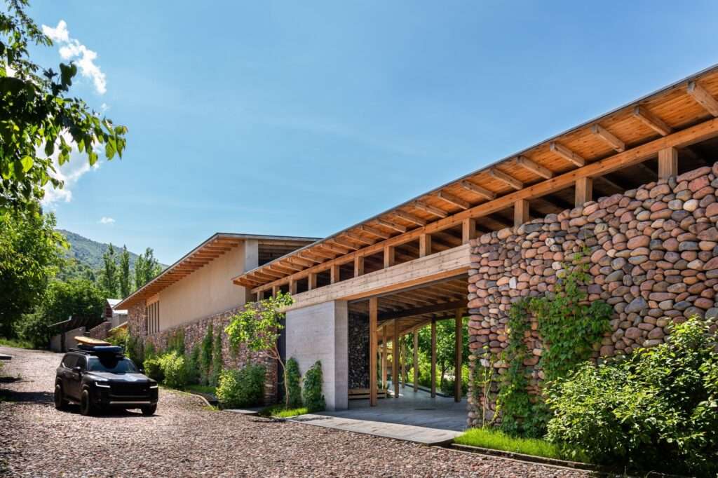 Exterior stone façade wall and timber roof structure of Buladala House along a cobblestone approach road with a vehicle parked nearby.