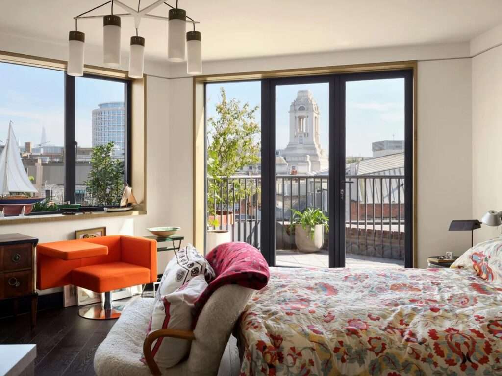 Bright bedroom interior with colorful bedding, designer armchair, and glass doors opening to a private balcony.