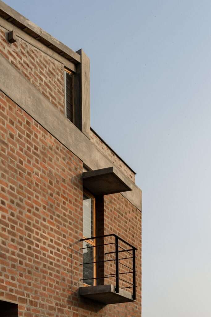 Architectural detail of a cantilevered concrete balcony with thin black metal railings jutting out from an exposed red brick facade.