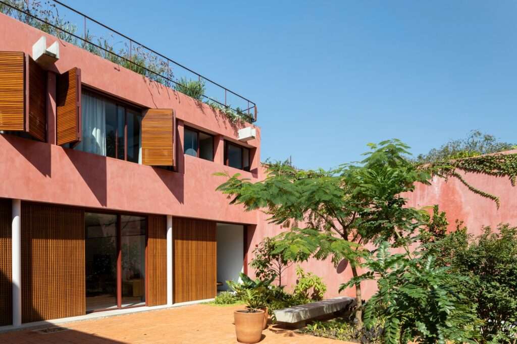 Central open courtyard with brick paving, planted trees, concrete bench, and floor-to-ceiling sliding glass doors opening to interior spaces.