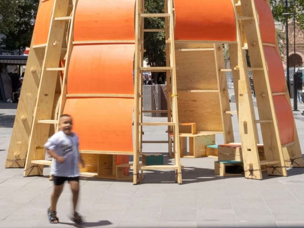 Child running past the entrance of the Paso Nara temporary timber structure in Plaza de Armas.