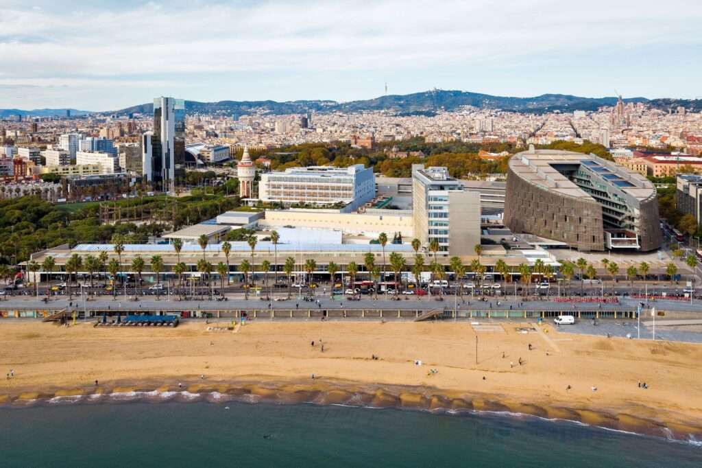 Panoramic aerial view of Hospital del Mar complex along the Barcelona coastline and beach promenade.