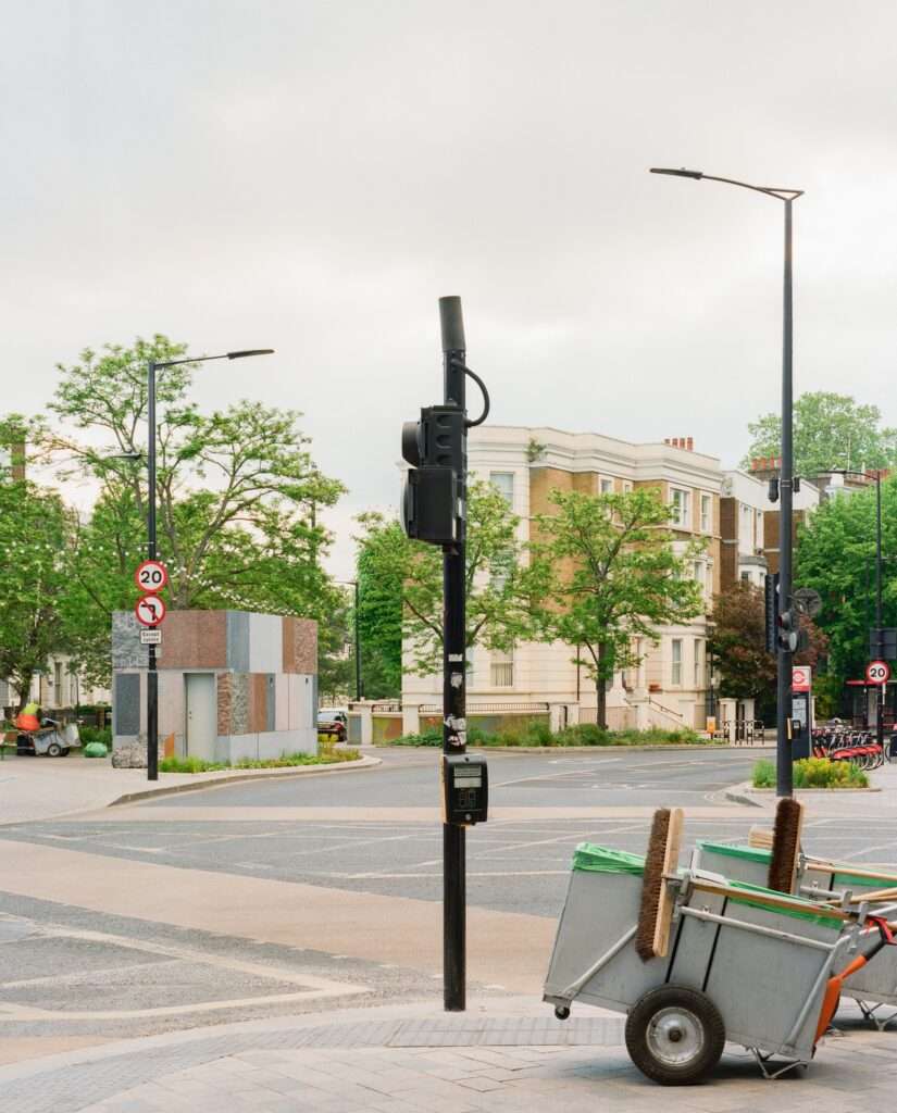 Street view of Maida Hill public toilet pavilion across a road intersection with street cleaning carts in the foreground.