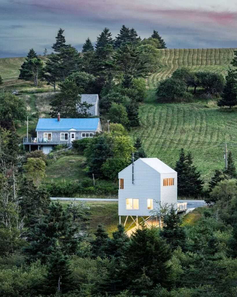 Distant aerial-angle view of the Skybox cabin nestled within a rolling green landscape near traditional rural structures.