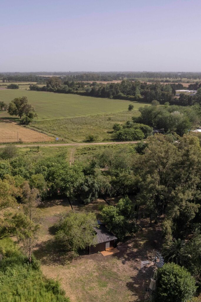 High aerial drone photo showing Etchegoyen House nestled inside a dense patch of trees surrounded by large agricultural fields.
