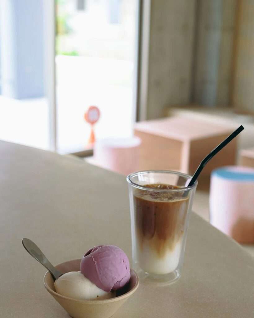 Close-up of ice cream bowl with two scoops and an iced latte beverage placed on the smooth counter surface.