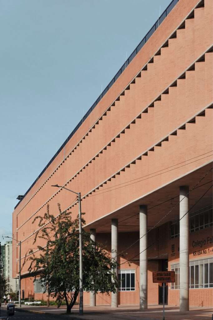 Low-angle perspective of the main brick facade and tall concrete pilotis at the entrance of Feliza Bursztyn School.