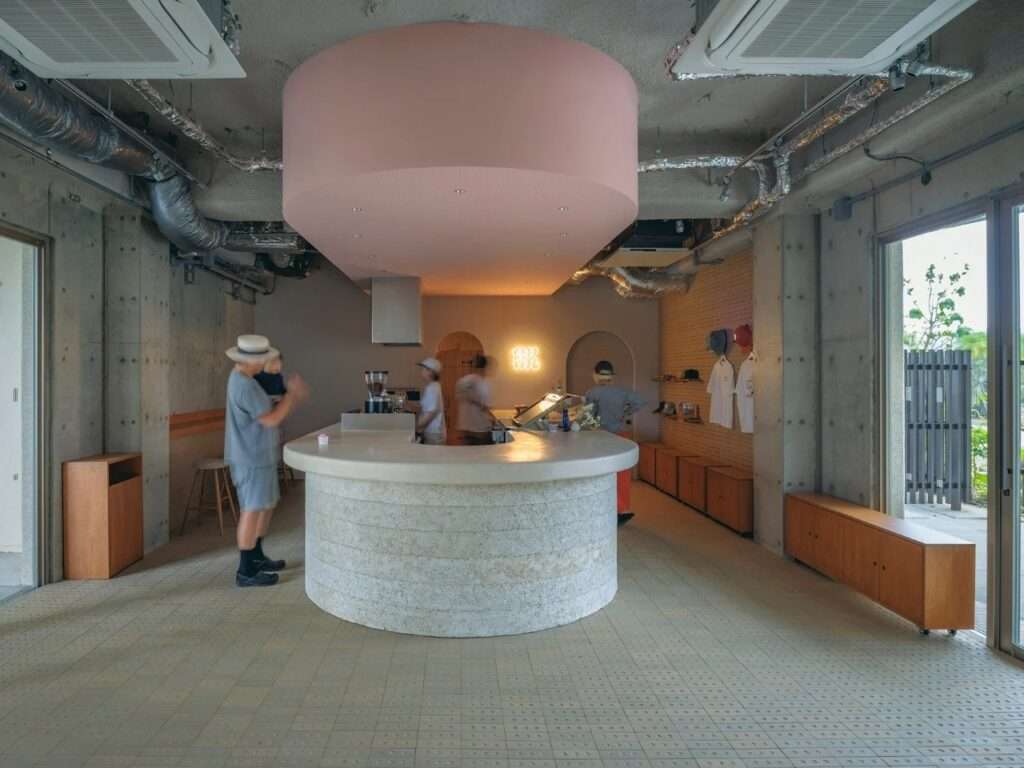 Visitors and staff interacting at the central curved lime plaster counter under the pink suspended ceiling.