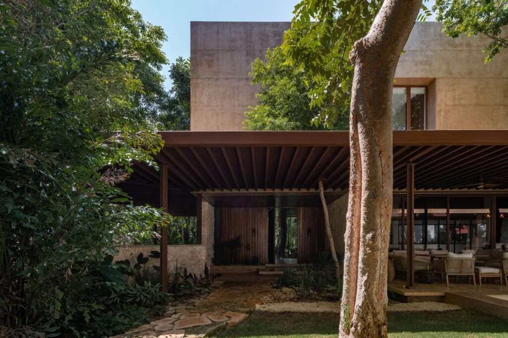 View from the garden toward the shaded terrace showing wooden columns, stone walls, and surrounding tree canopy.