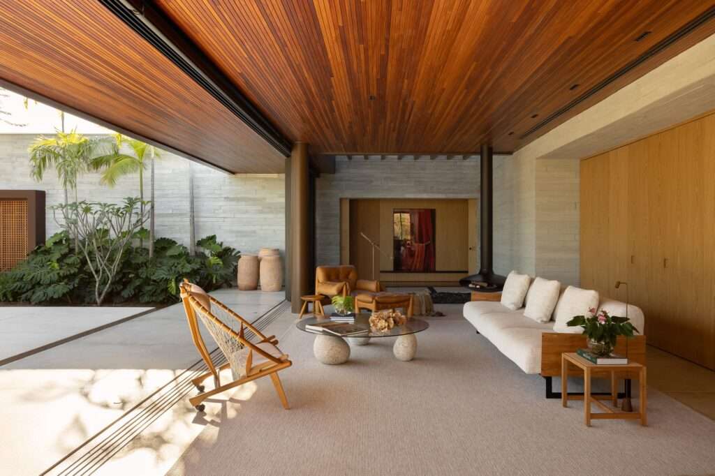 Interior living room of Casa da Mata with slatted timber ceiling, suspended black steel fireplace, cream sofa, and pocket doors opening to a lush courtyard.