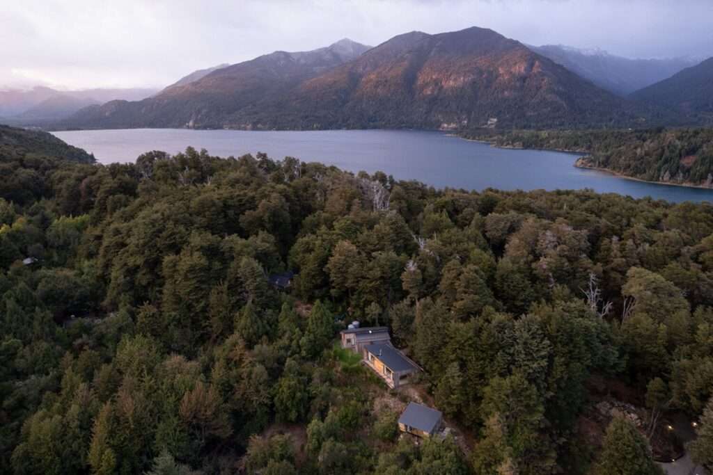 Aerial photograph of Casa El Trébol roof volumes nestled in dense forest above Lake El Trébol with mountain backdrop.