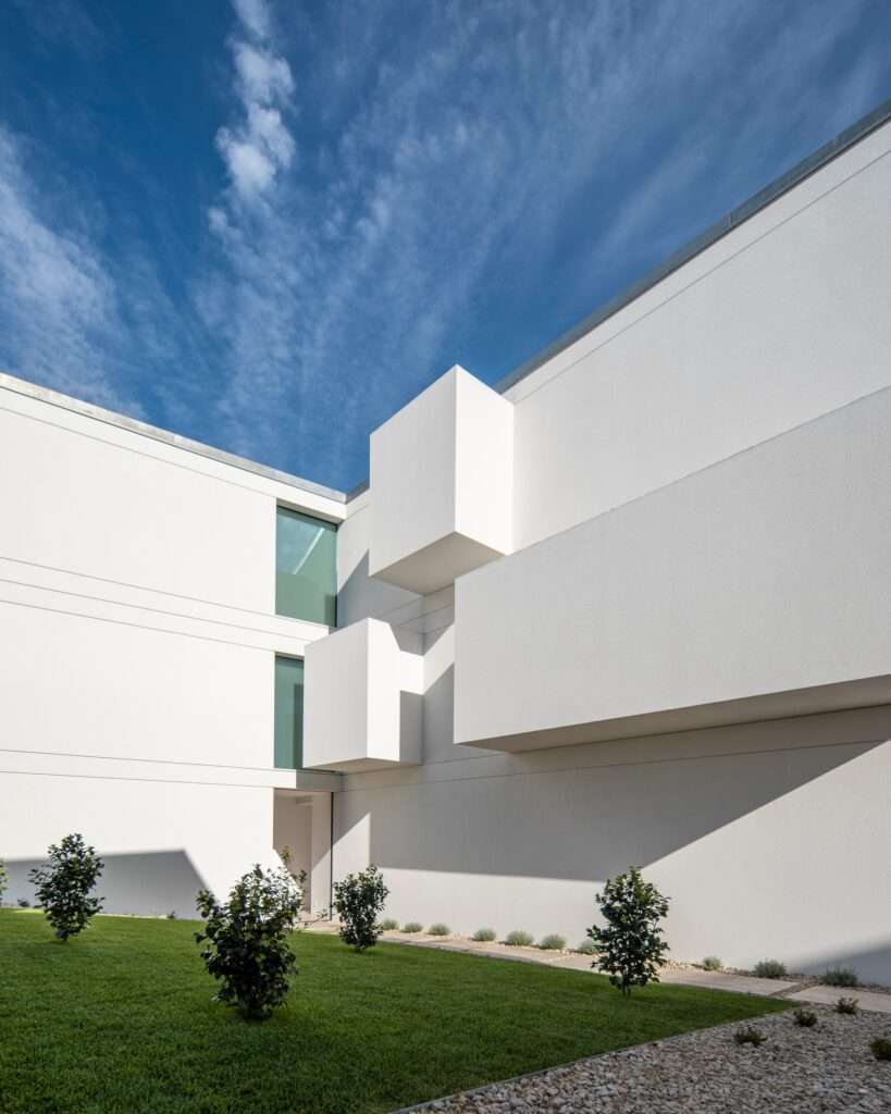 Low-angle shot of a white modern building facade with protruding volumetric balconies overlooking a green lawn.