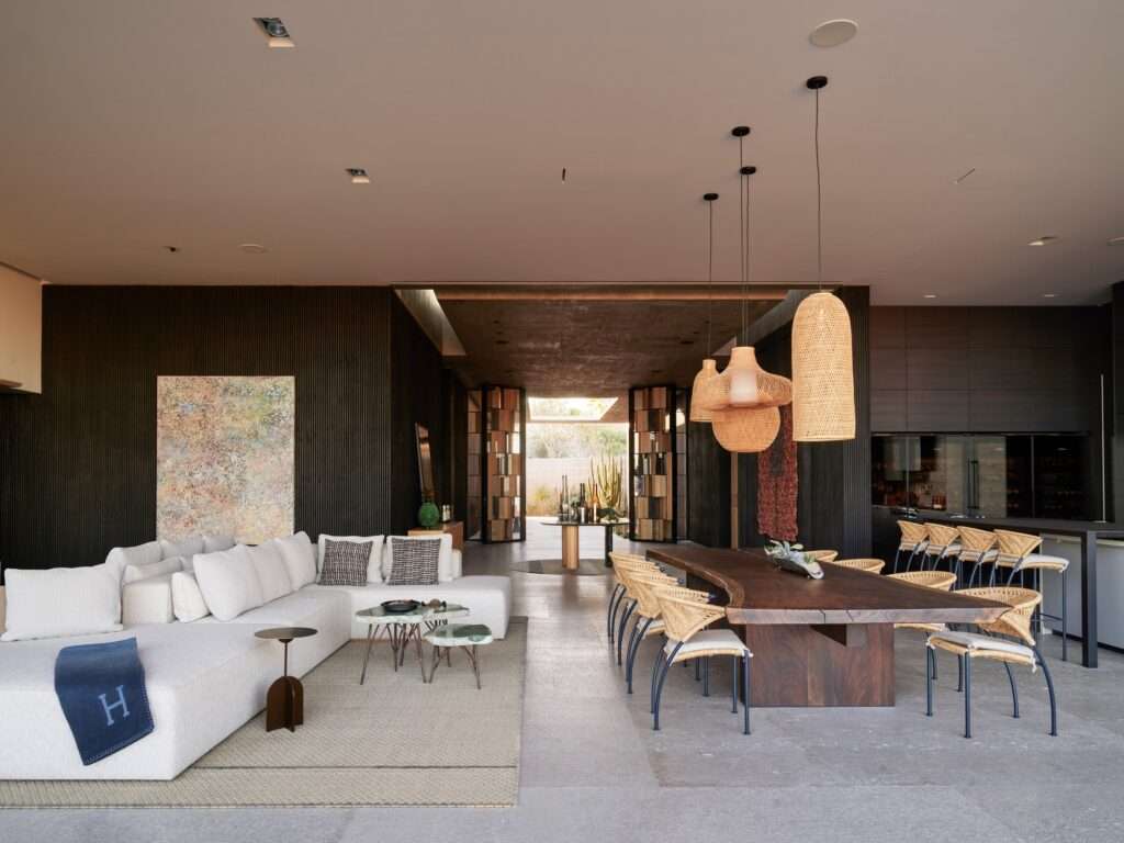 Open-plan main living room and dining area with wooden table, woven pendant lights, large sofa, and dark wall surfaces.