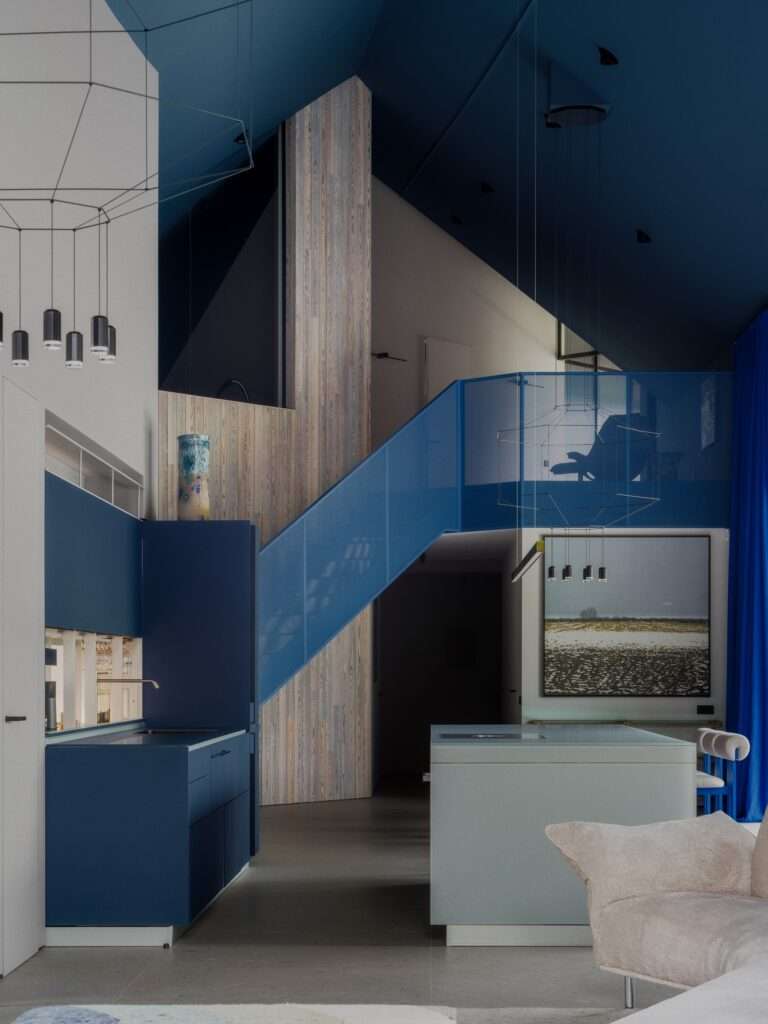 Double-height interior living area featuring a deep blue vaulted ceiling, blue mesh metal staircase, and open-plan kitchen island.