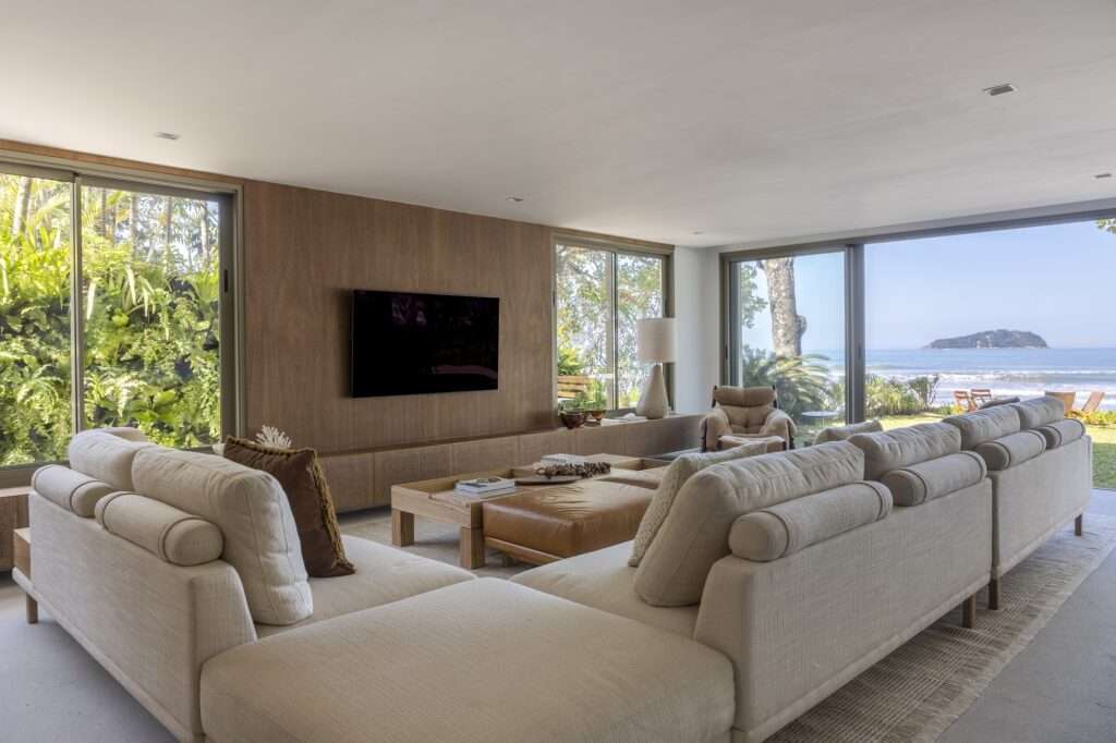 Living room in Casa ADS featuring a large modular sofa, wooden media wall, indoor greenery view, and panoramic ocean vistas.