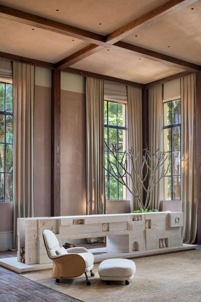 Detailed side angle of a hand-carved travertine fireplace adorned with carved relief motifs and an armchair with footrest.