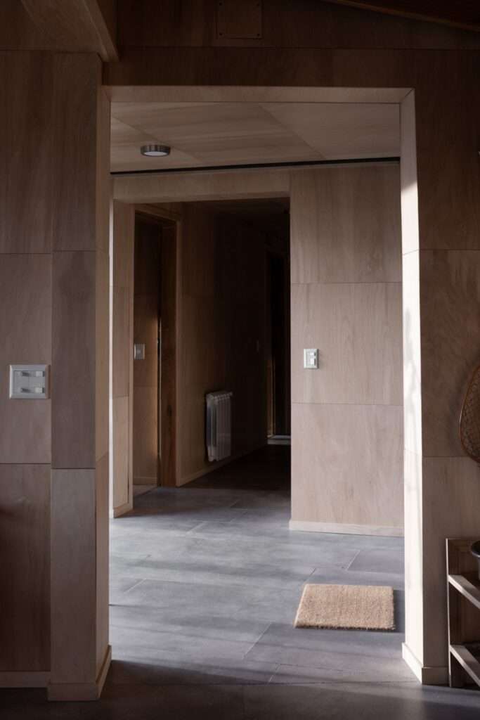 Minimalist interior hallway lined with light Guatambu wood paneling and grey stone floor tiles in Casa El Trébol.